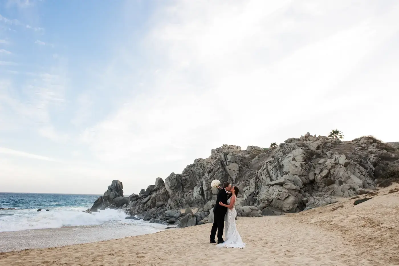 Couple kissing on rocky cliffs during couples session in Cabo San Lucas