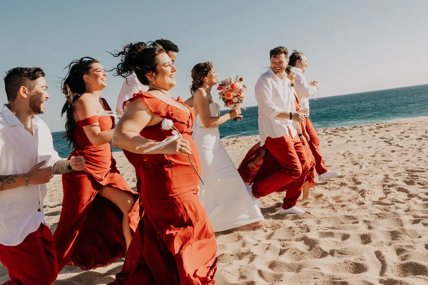 Cortejo nupcial con vestidos rojos en la playa