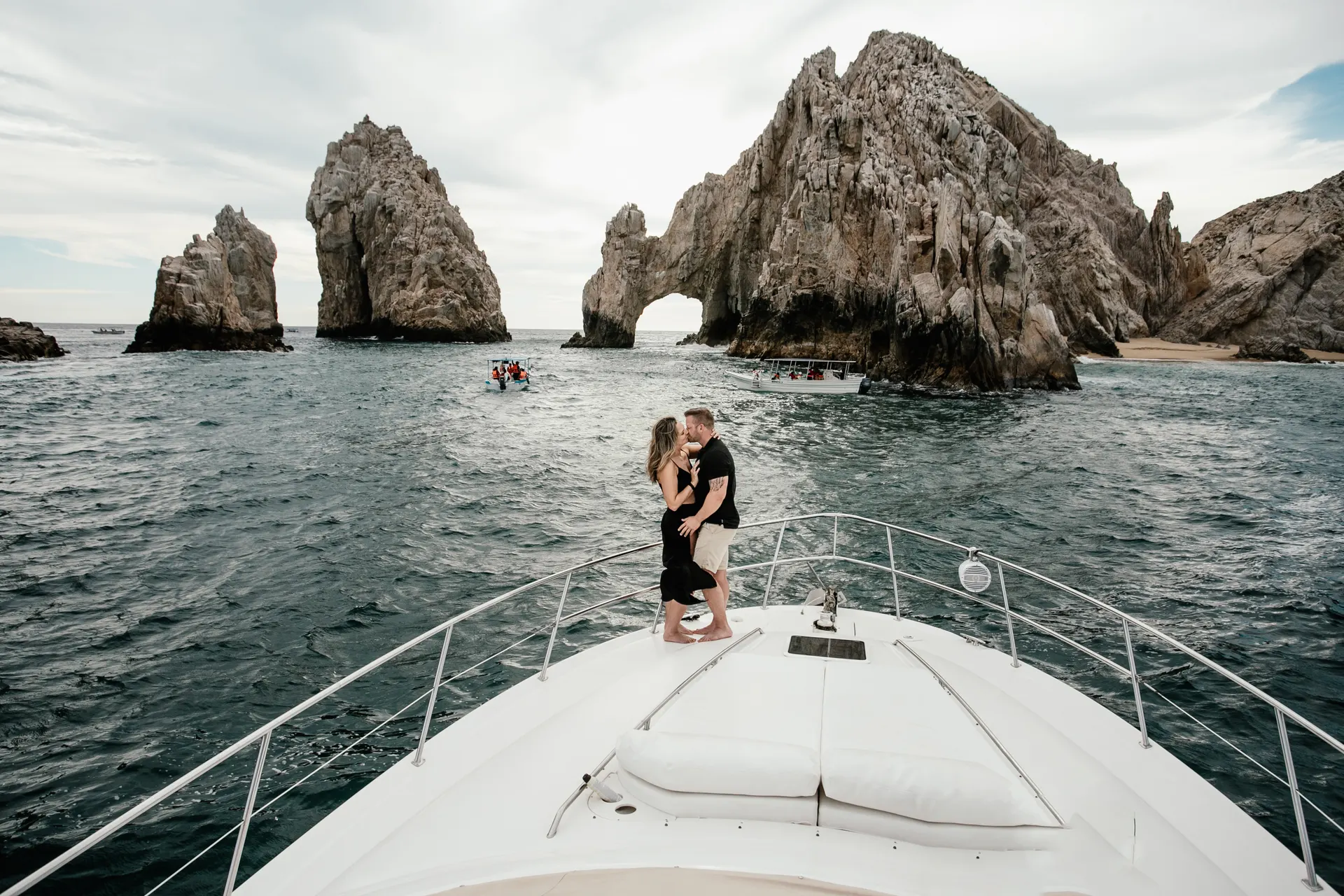 Couple kissing on the bow of a yacht in front of El Arco at Land's End in Cabo San Lucas, photographed by Ana Badillo