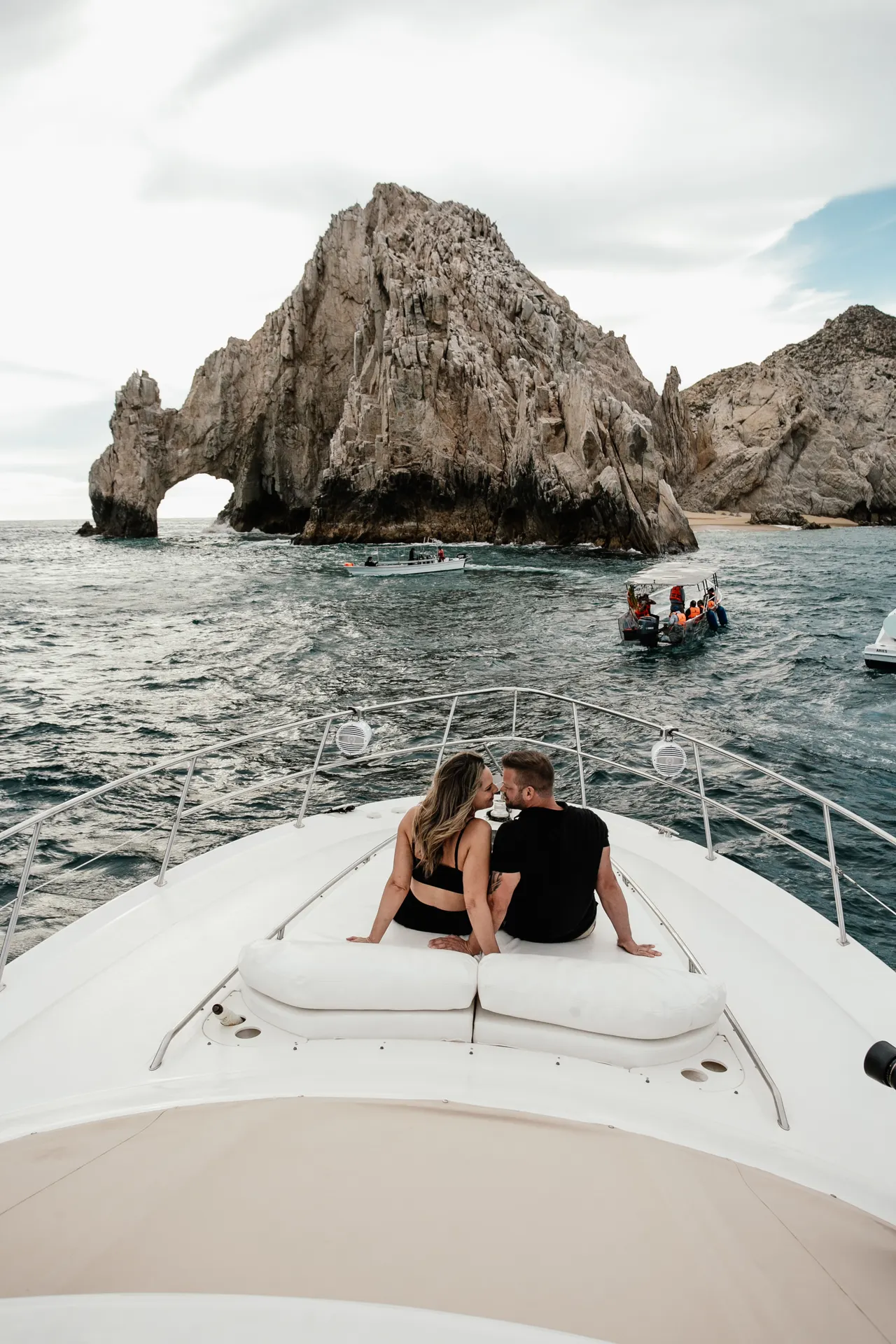 Couple relaxing on the bow cushions of a yacht facing El Arco in Cabo San Lucas